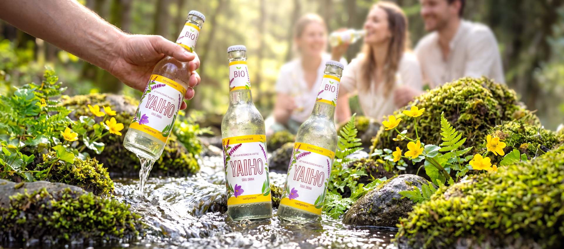 YAIHO Bio Soul Drink im klaren Bachwasser mit Freunden im Wald und erfrischend natürlichem Ayurveda-Genuss